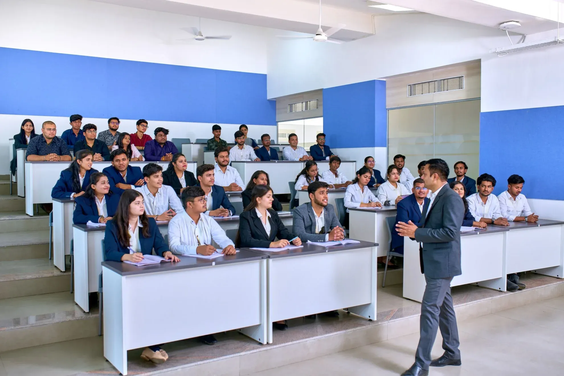 A class in session, with a lecturer walking the lengths of the classroom.